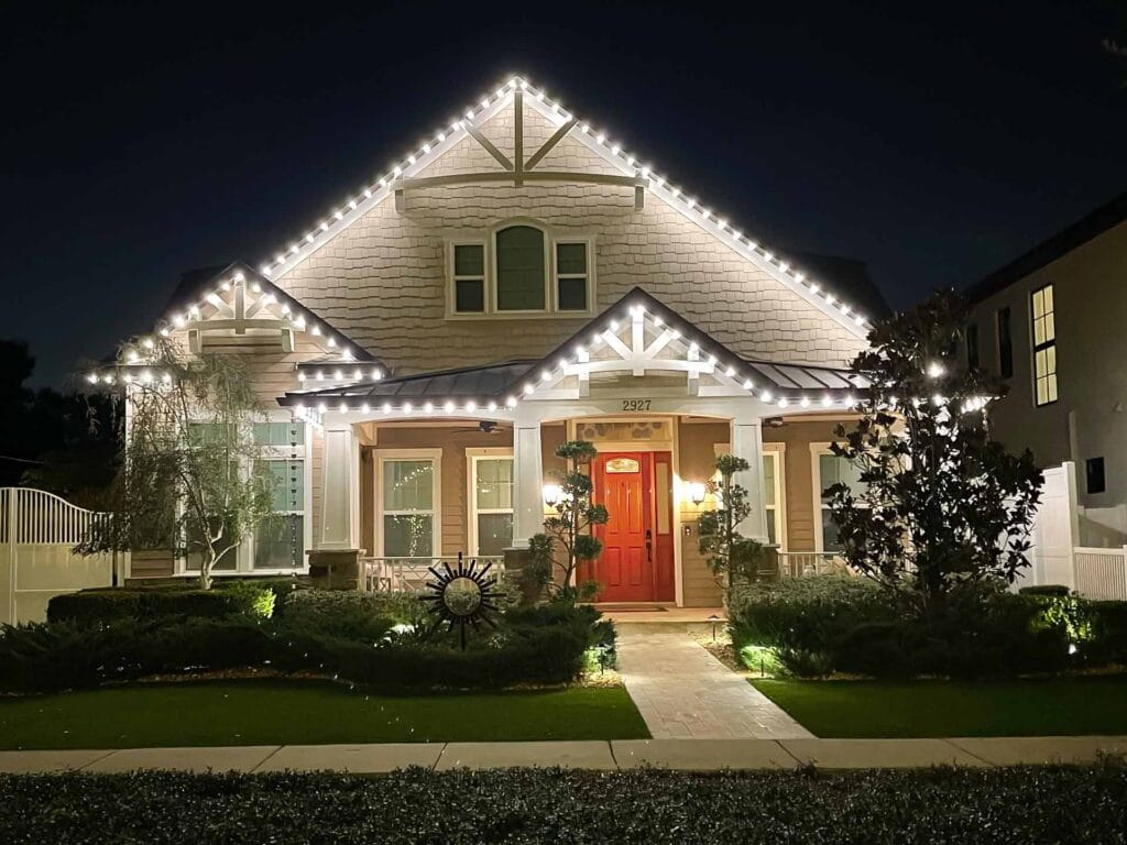 A house at night with christmas lights outlining the roof, a red front door, and well-kept landscaping in the front yard.